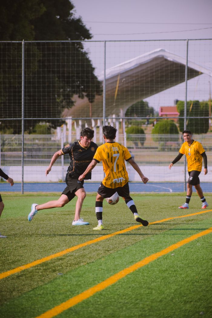 Teenagers playing soccer on a sunny day on an outdoor field.