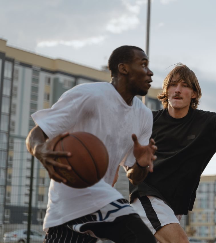 Two men engaging in a competitive basketball match outdoors on an urban court.
